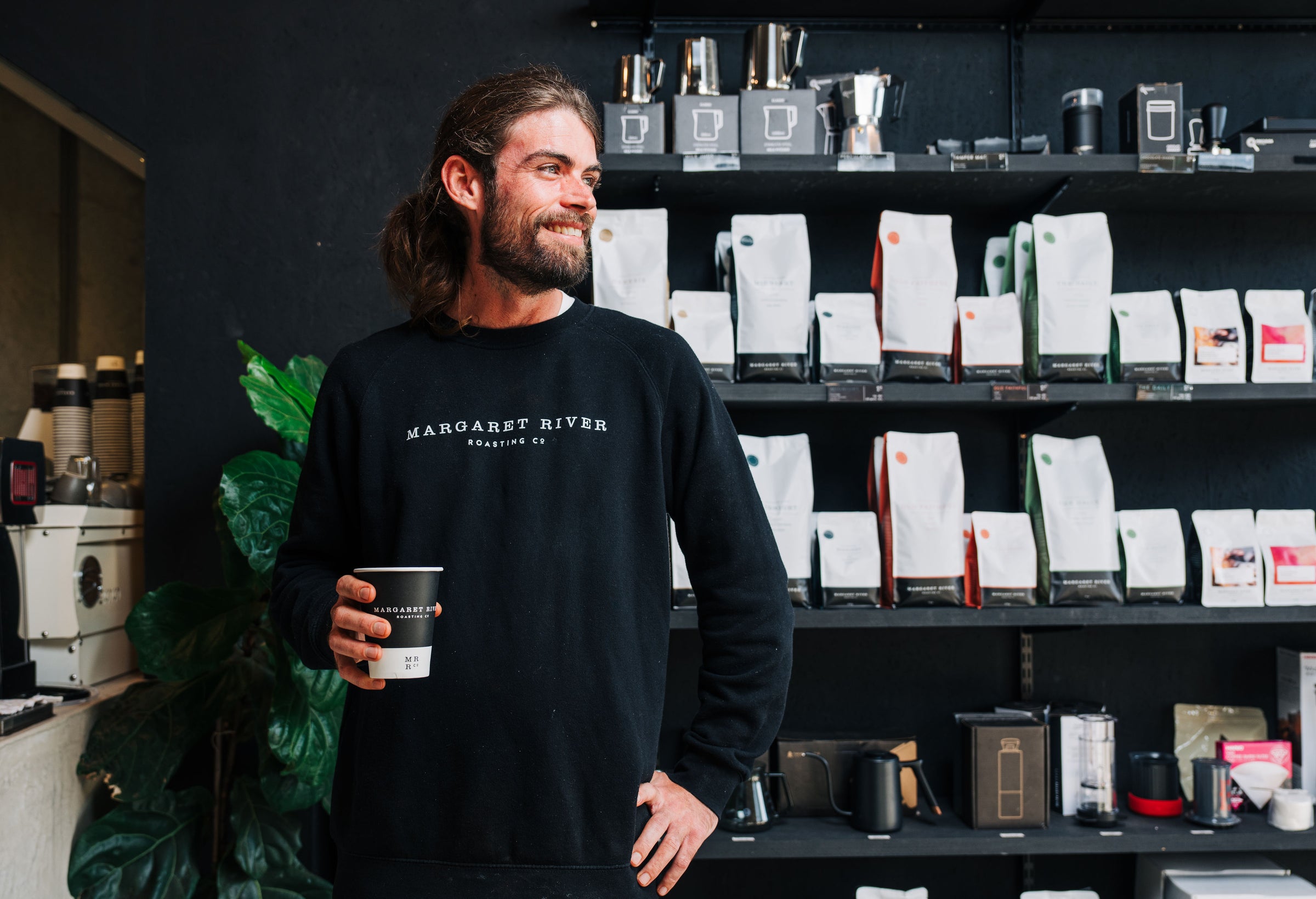 white male with ponytail holding a cup of roasted coffee